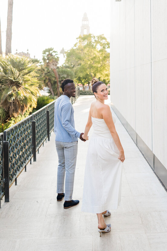 engaged couple walking toward bell tower Balboa Park