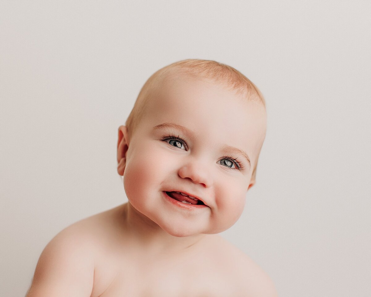 Baby reaching toward camera with curious expression during milestone session