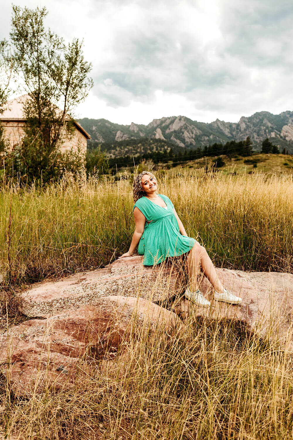 Senior girl sitting on rocks in a field in the mountains of Boulder.