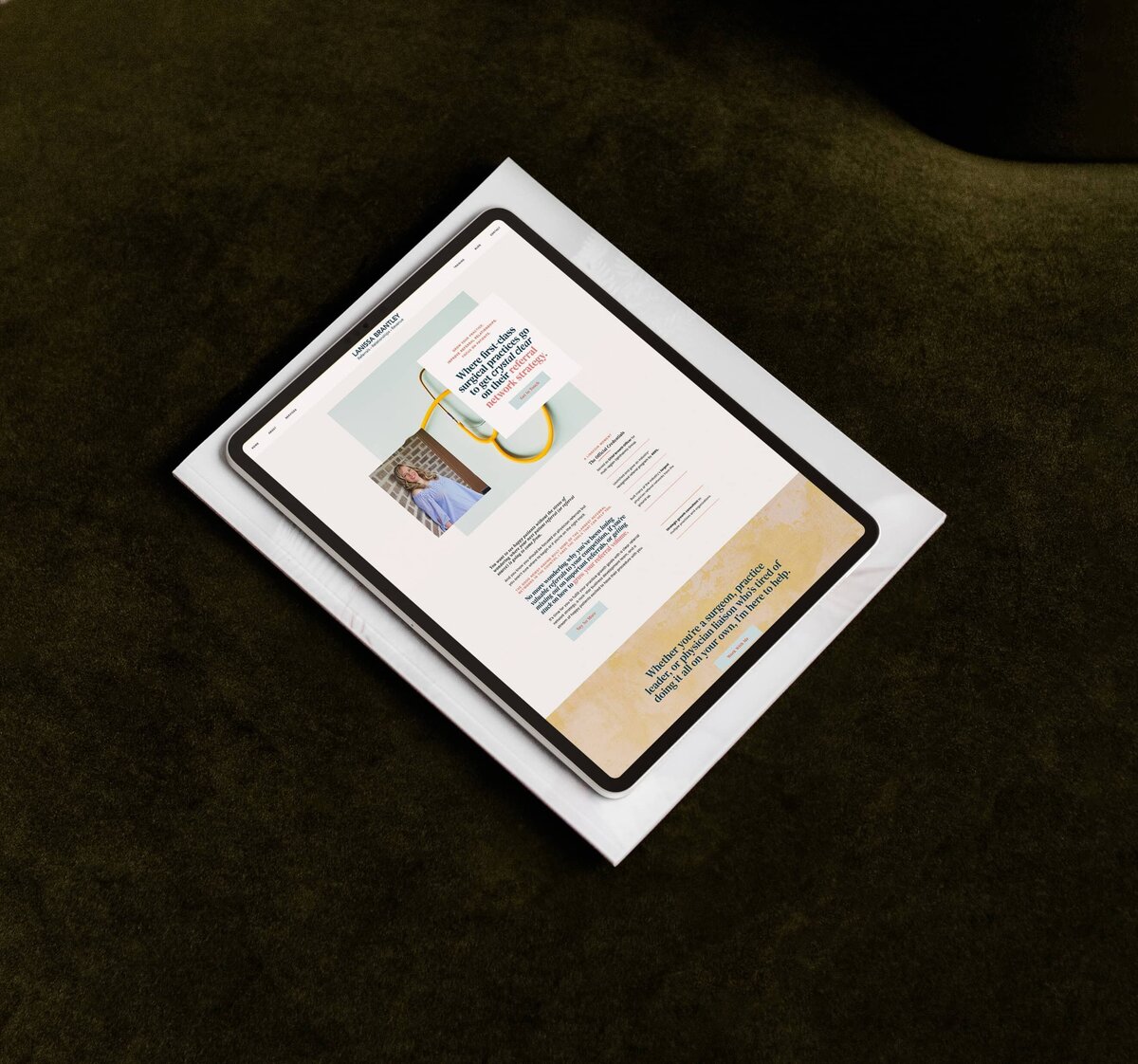 A tablet displaying a showit website for personal brands rests on top of a closed hardcover book on a dark green surface.