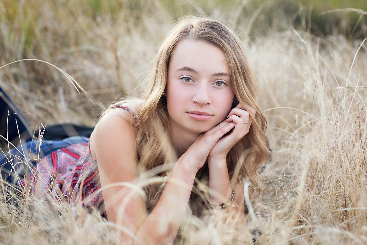 Teen girl in tank top poses for her senior photo session in a grassy field