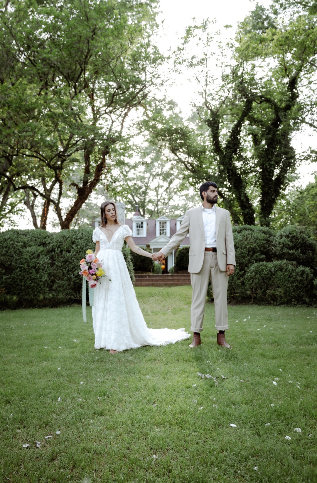 Groom sitting on a tree branch while bride rests her head on his shoulder, holding a vibrant bouquet.