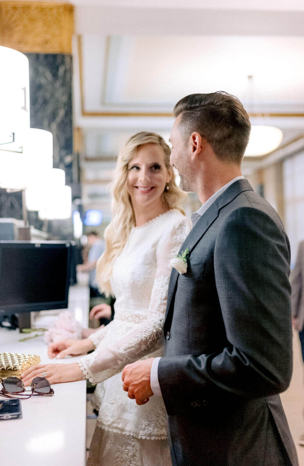 The bride and groom are happily looking at each other on a counter in NY City Hall for their elopement. Image by Jenny Fu Studio