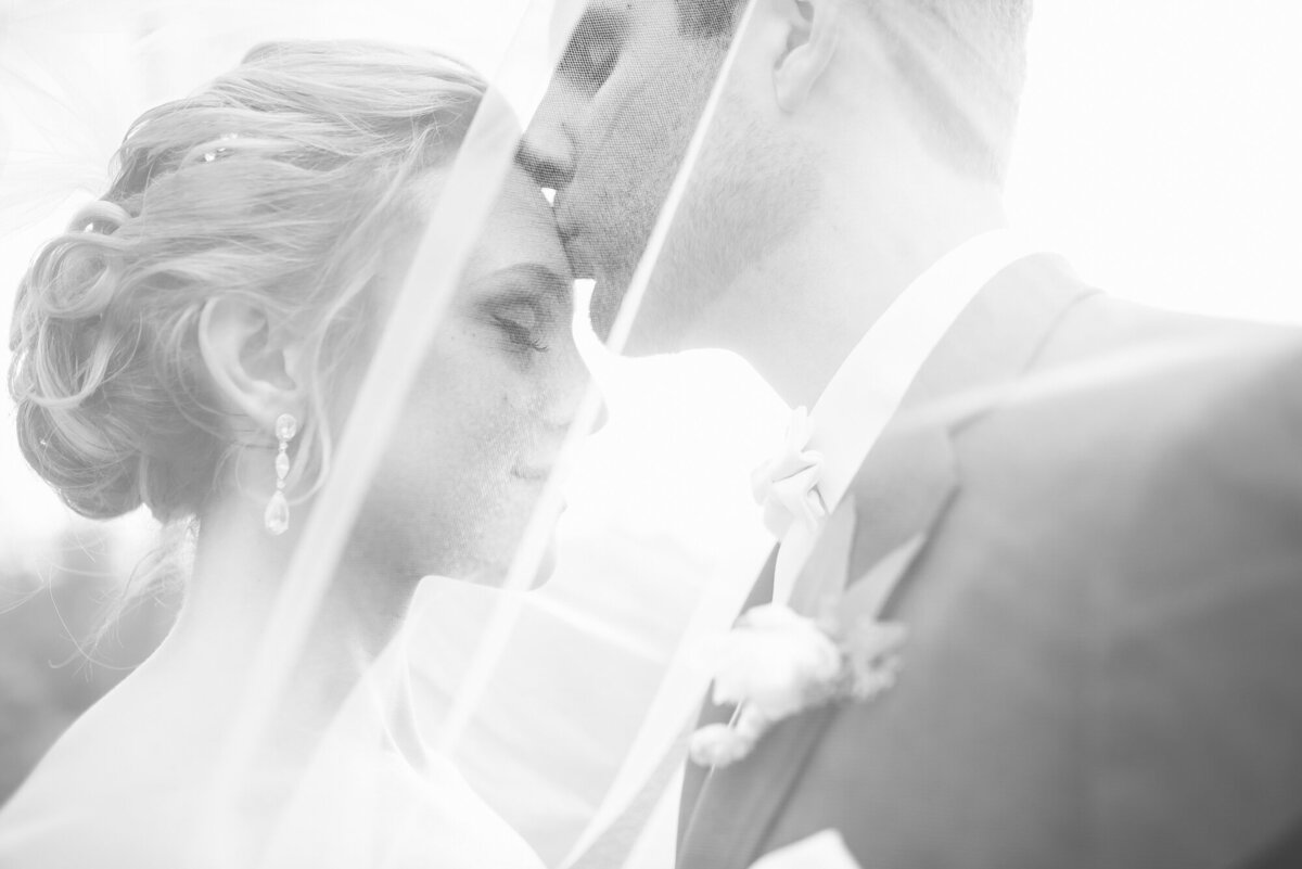 Black and white wedding photo of bride and groom under veil in emotional embrace – Kari Dawson + Co Signature Work