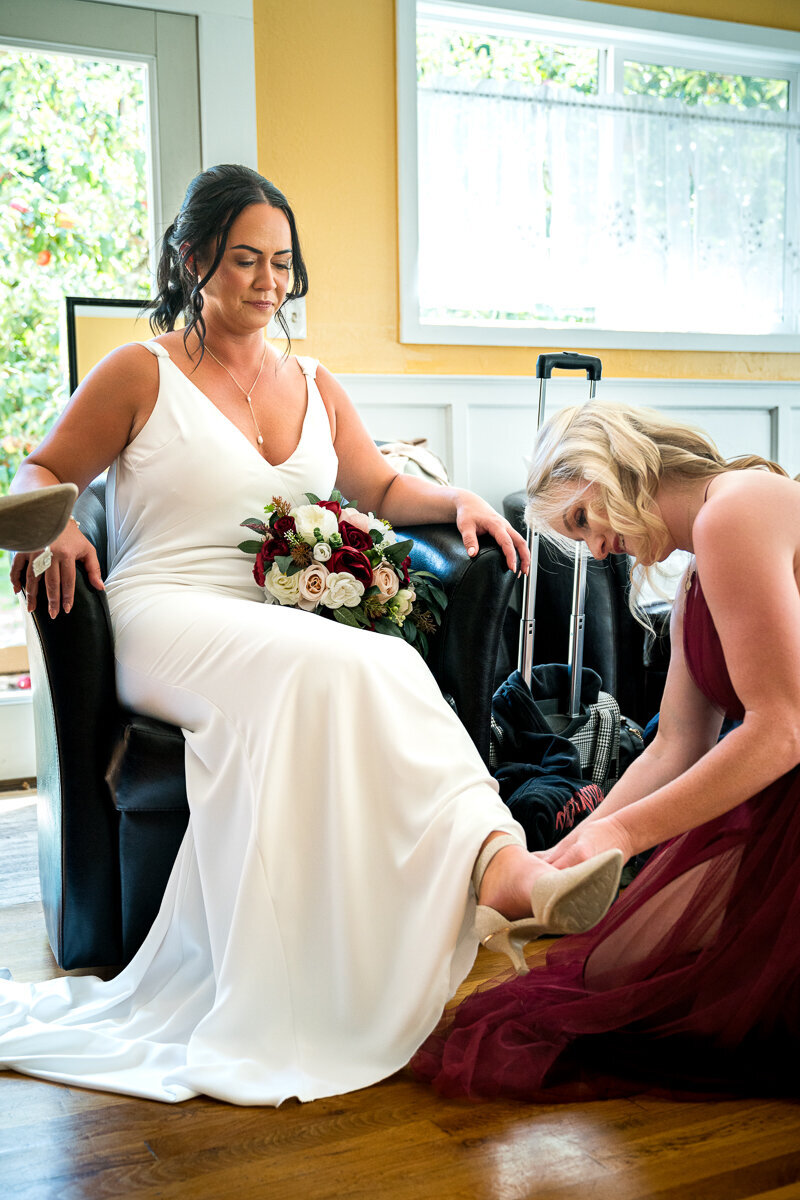 A heartfelt moment as the bridesmaid gently helps the bride put on her shoes in the serene setting of Mitchell Grove. This intimate wedding day detail showcases the bond between the bride and her closest friends, surrounded by the natural beauty of Eureka, California.
