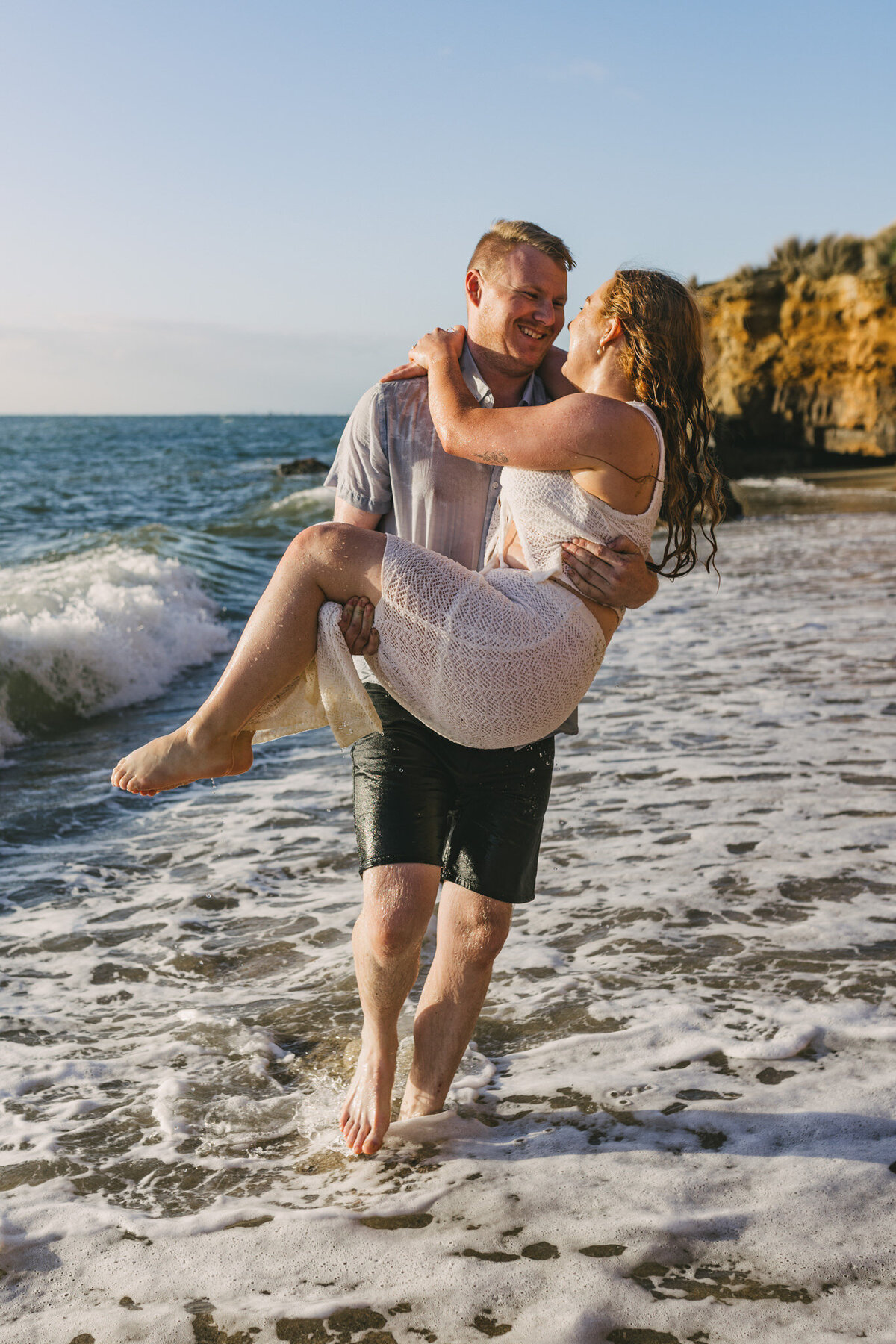 Male is carrying his Fiancé with her legs draped over his arms. Both are soaking wet and laughing, enjoying this emotion-filled moment captured by a Bendigo Wedding Photographer. 