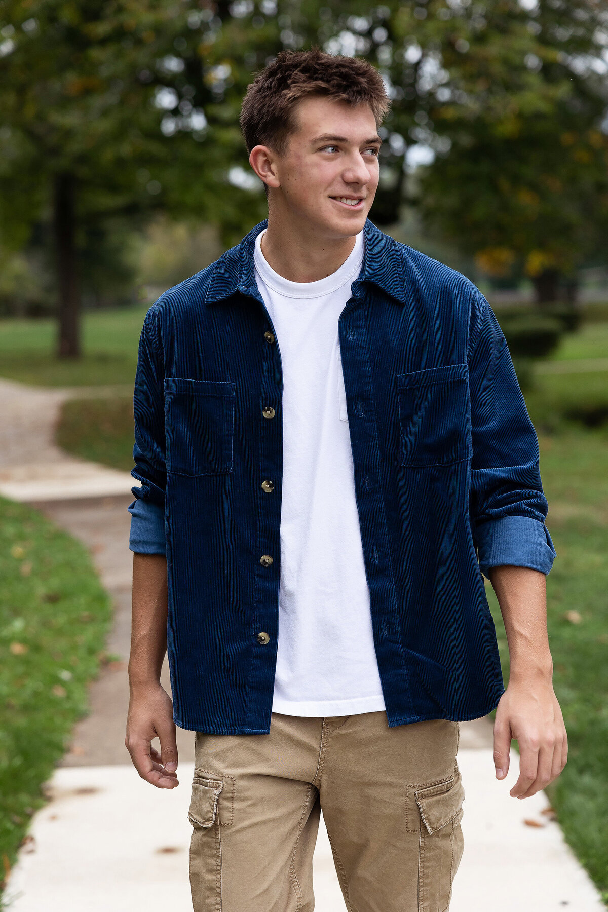 Highschool senior is walking looking away in blue button down shirt in Greensburg pa.