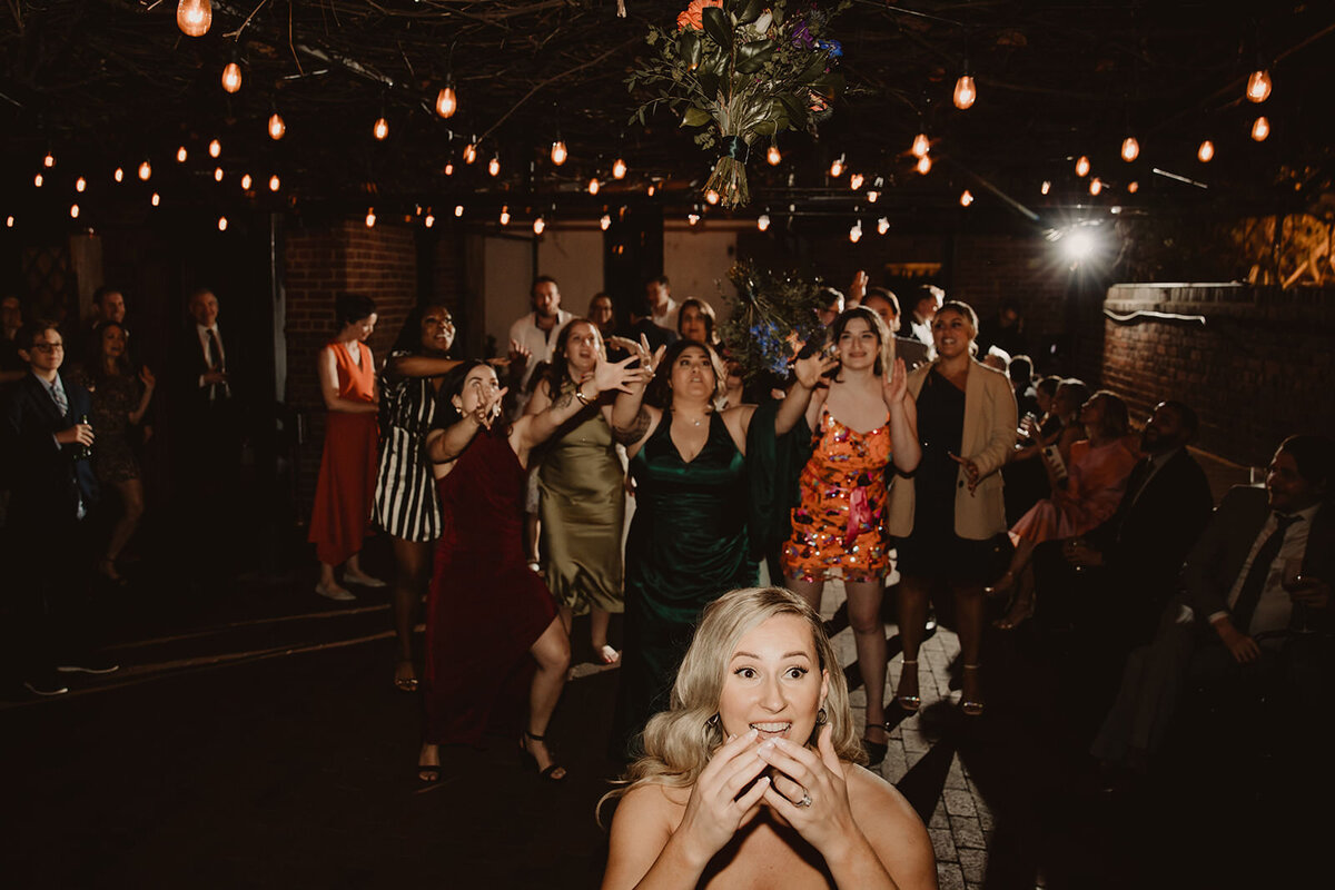 A newlywed throwing their bouquet over their head to waiting guests 