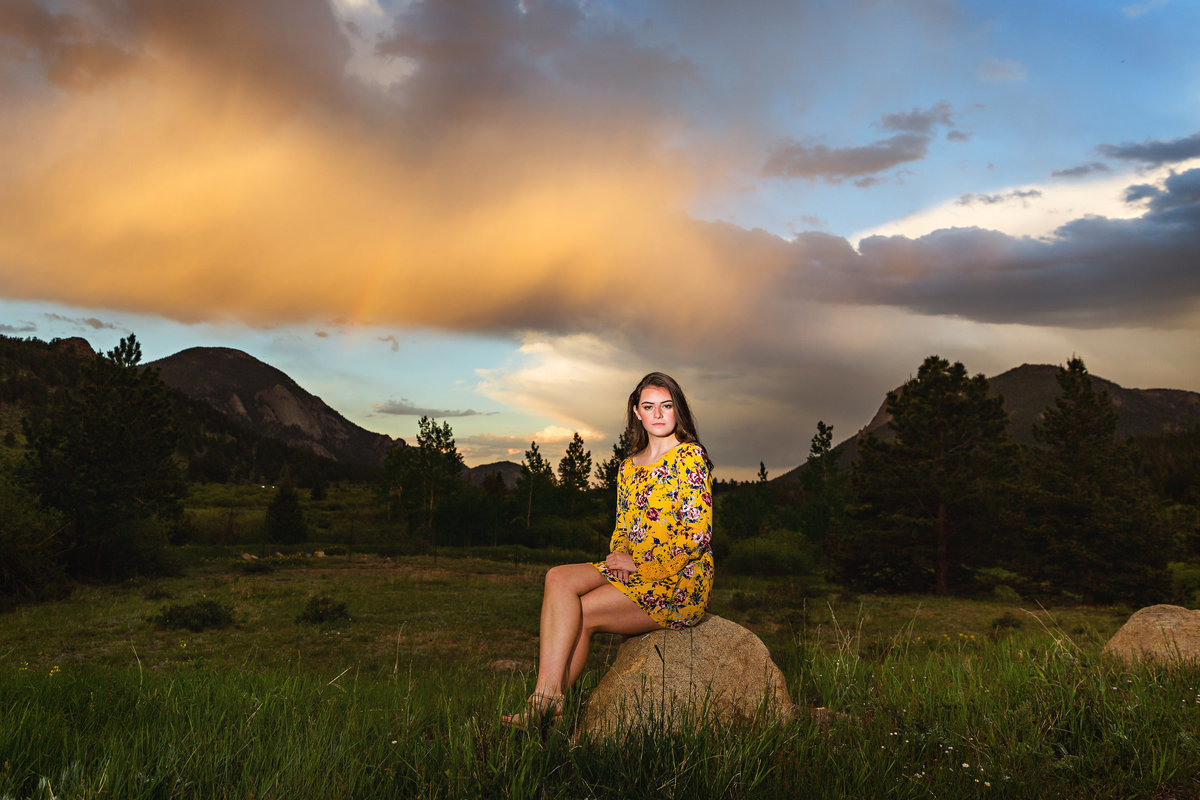 Girl in a yellow romper poses for her senior photos in a meadow at sunset