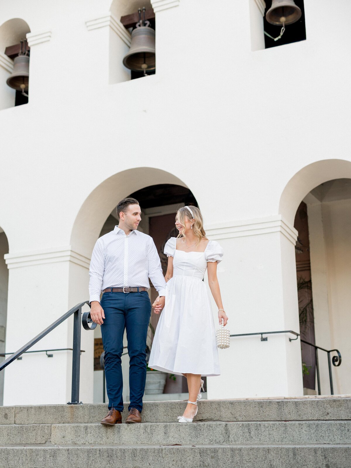 Romantic engagement session at the San Luis Obispo Mission—elegant couple holding hands beneath classic white arches.