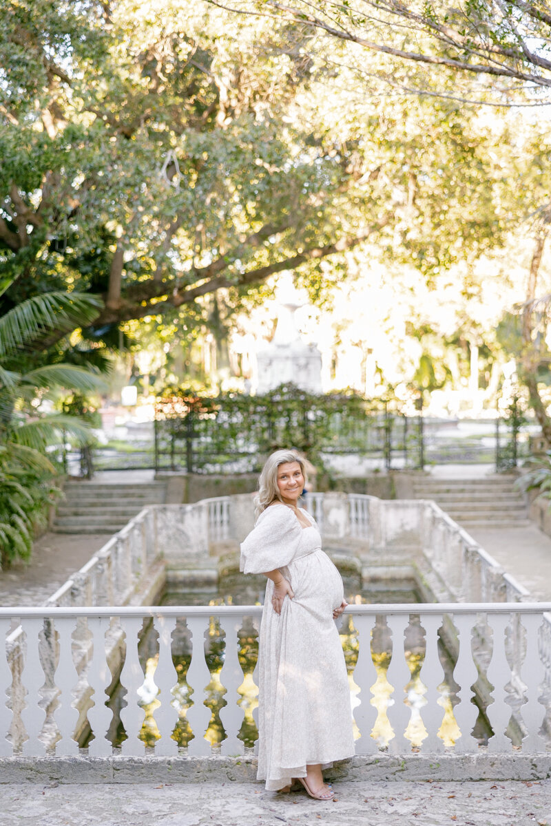 A mother-to-be cradles her baby bump amidst lush greenery.
