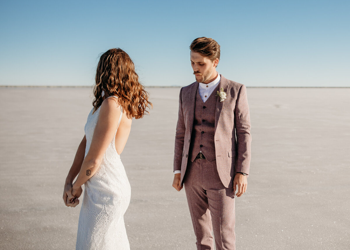 A bride and groom standing on a vast salt flat, facing each other with a clear blue sky above
