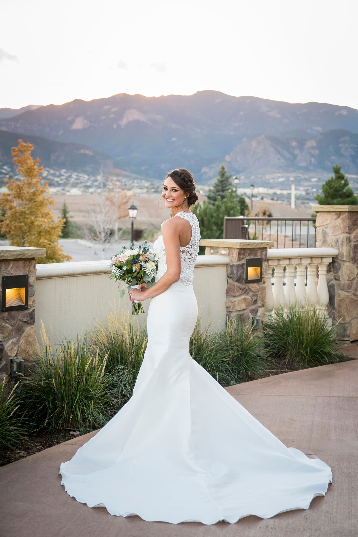 A bride looks over her shoulder, smiling at the camera with the Colorado landscape in the the background.