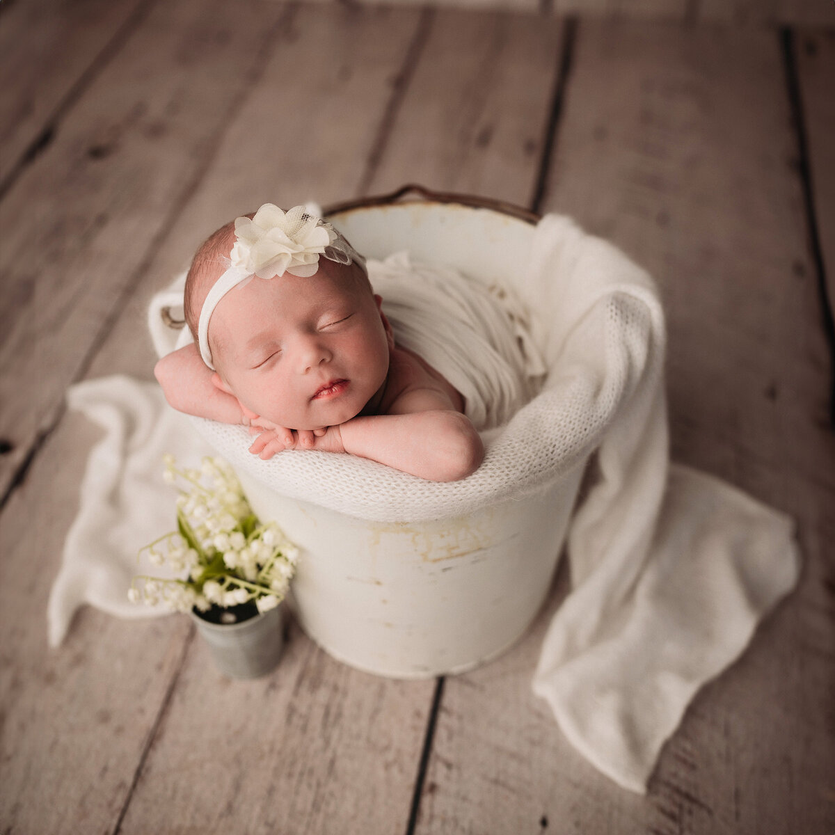 sleeping newborn baby girl with white tieback posed with hands on chin over the