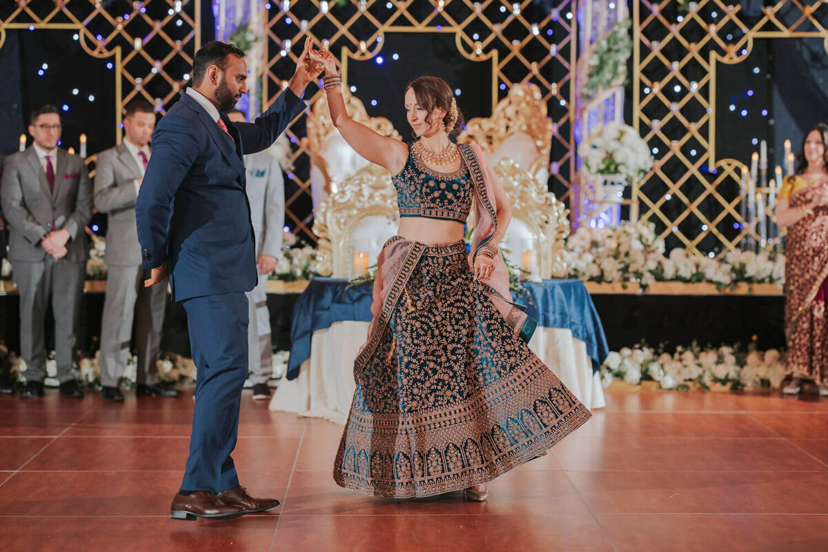 A couple gracefully dances on a vibrant reception stage adorned with golden accents, floral arrangements, and twinkling lights. Wedding at The Philadelphia Downtown Marriott. 