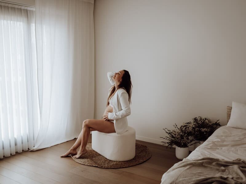 Een dromerige zwangerschapsfoto in een lichte studio in Beveren. De vrouw rust haar hand op haar buik en straalt vertrouwen, rust en verbondenheid uit.