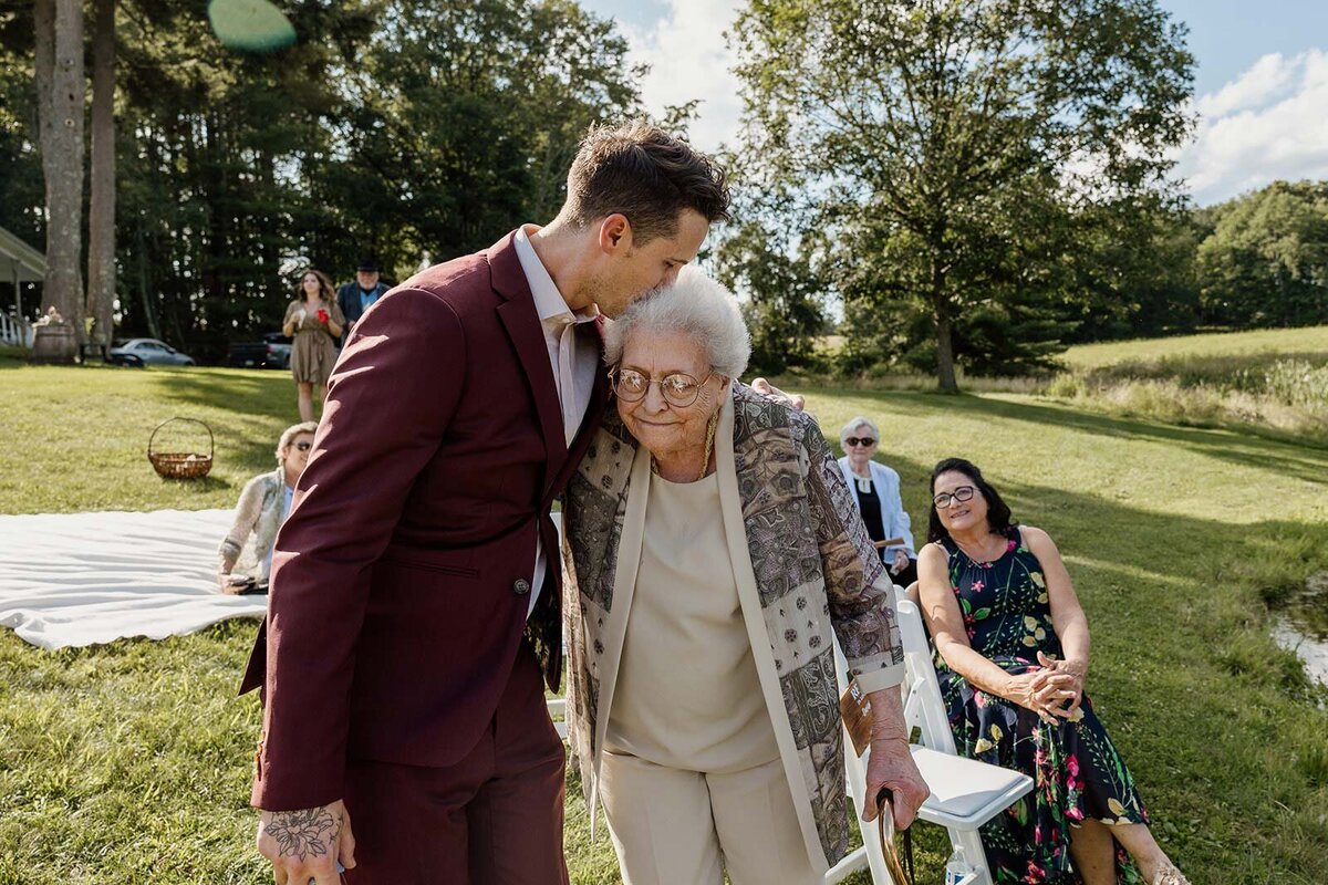 A groom kisses the forehead of the brides grandma during his wedding ceremony.