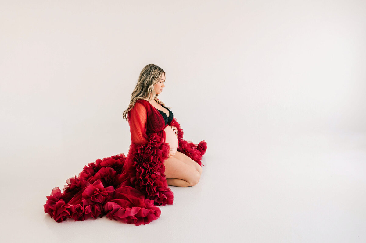 pregnant mom kneeling on floor holding baby bump during Springfield MO maternity photography session