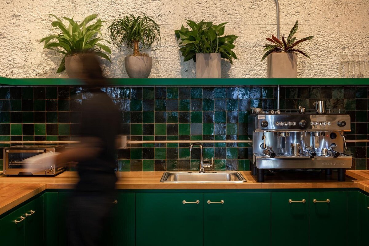 Office kitchenette with deep green cabinetry, wood countertops, emerald tile backsplash, and a commercial espresso machine.