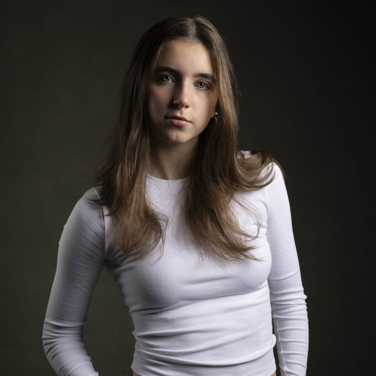 Studio headshot in MA of young woman in white long-sleeve shirt, posing confidently against dark background by Rob Faber Photography.
