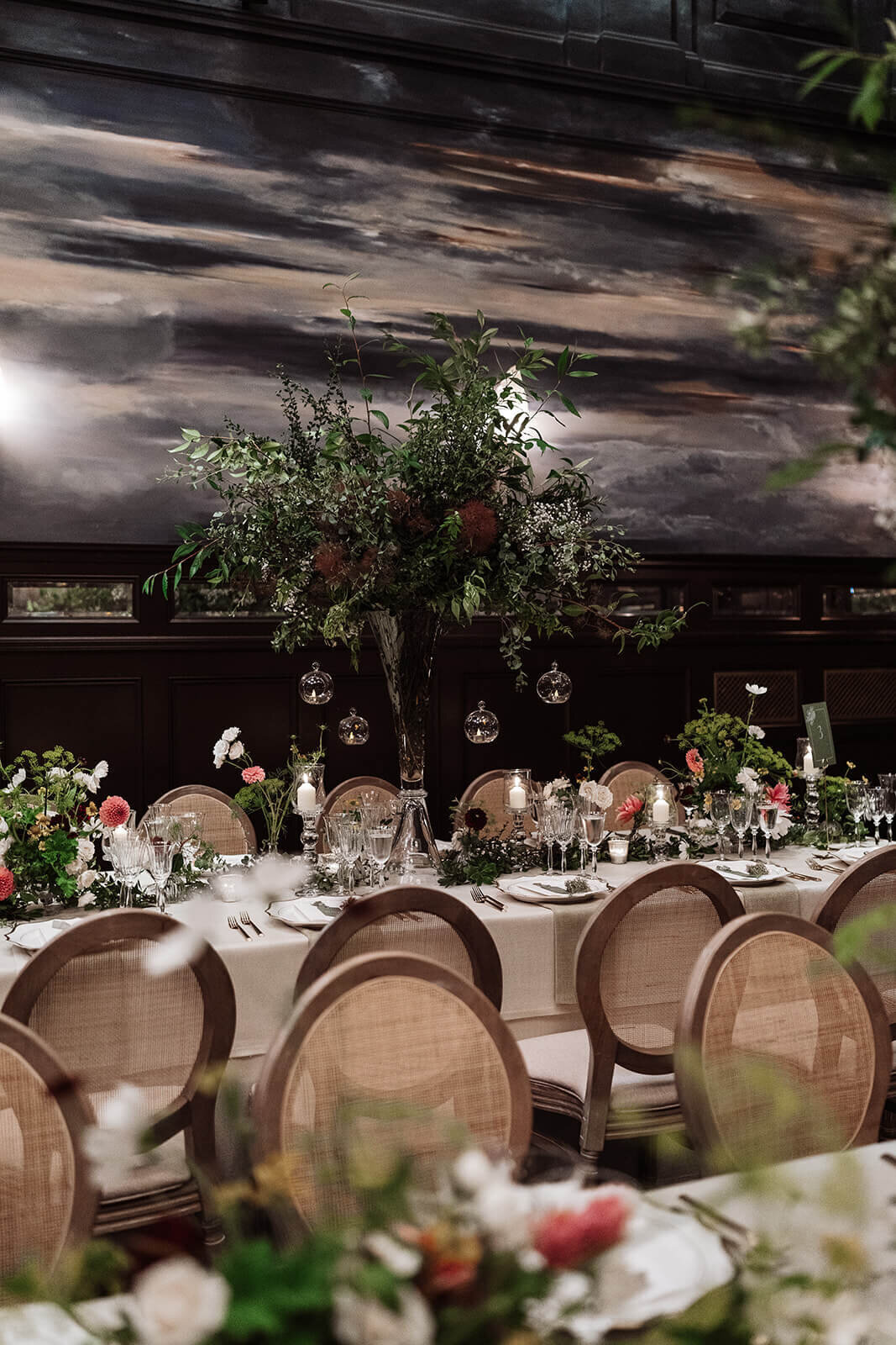 wicker round back chairs along long dining tables with trees as centrepieces for an intimate wedding in the ballroom at the nomad hotel london