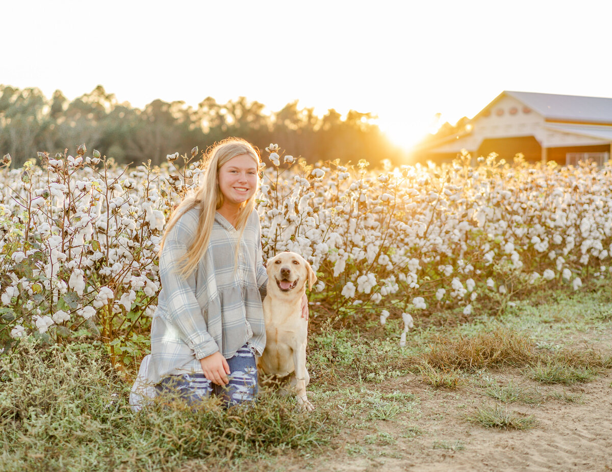 golden hour photo of child with her yellow lab while smiling in tall grass in front of cotton field