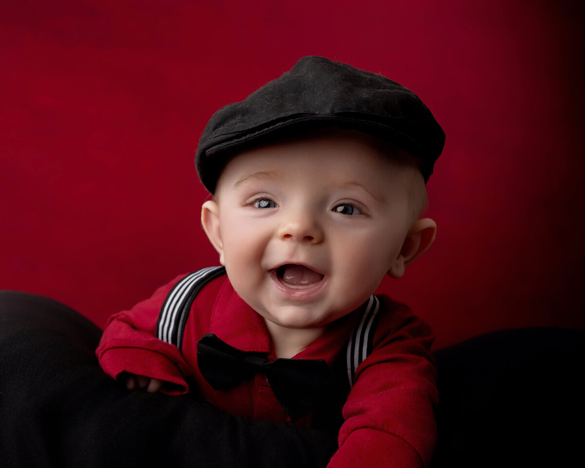Child in a red shirt and black cap smiles for his Iowa Milestone Photos