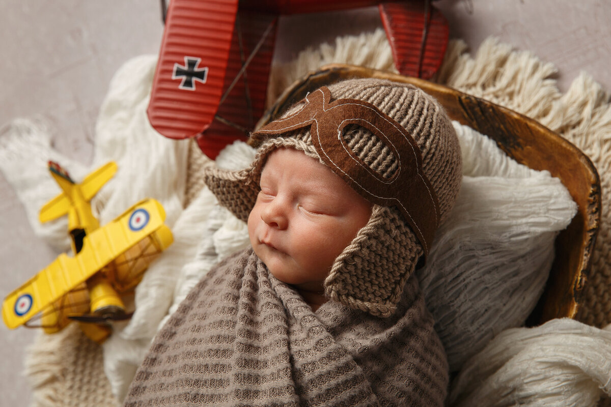 Closeup portrait of a newborn baby wearing a n aviator cap with toy airplanes