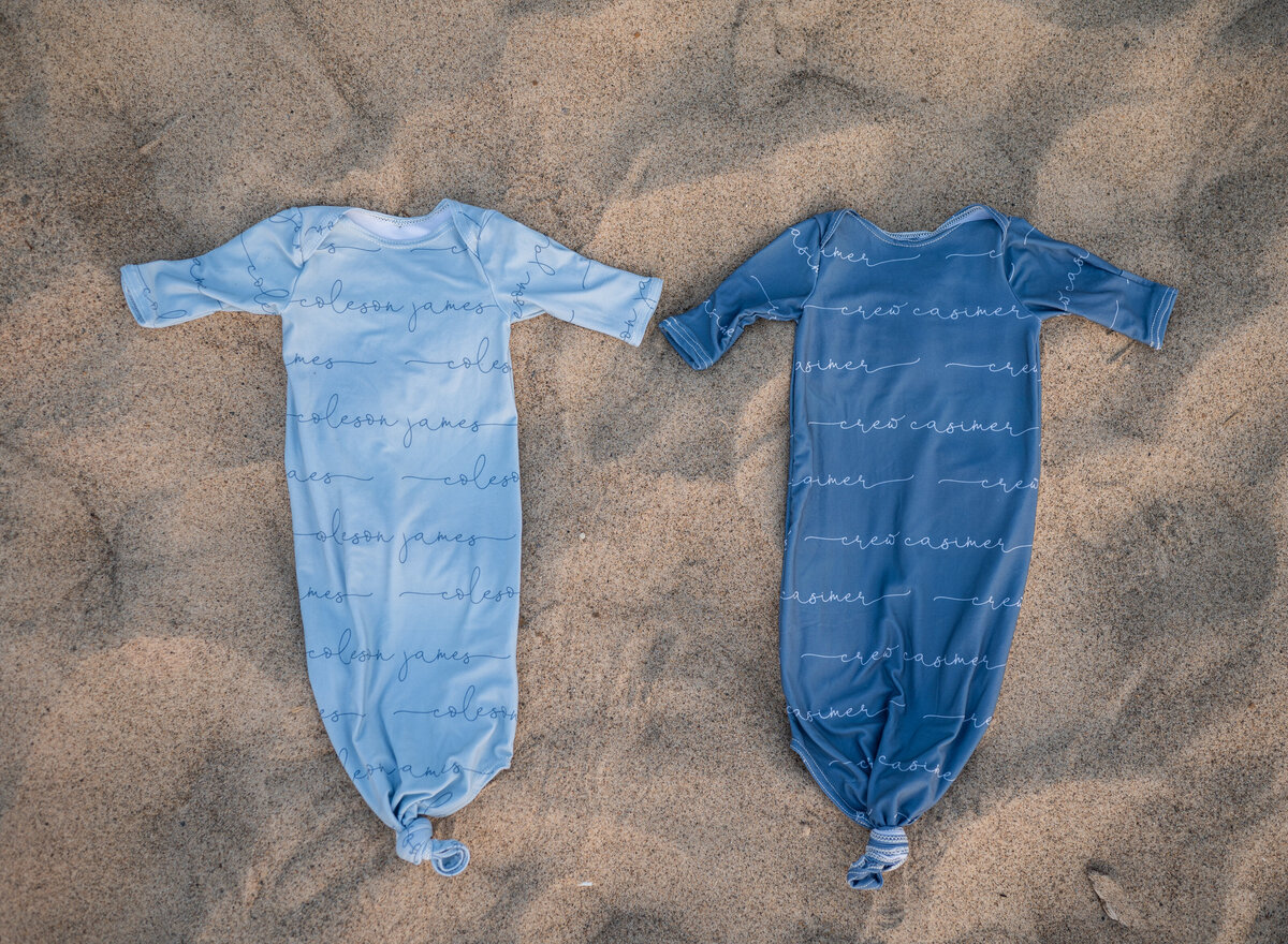 Two blue baby gowns laid side by side on sandy beach, ready for a newborn