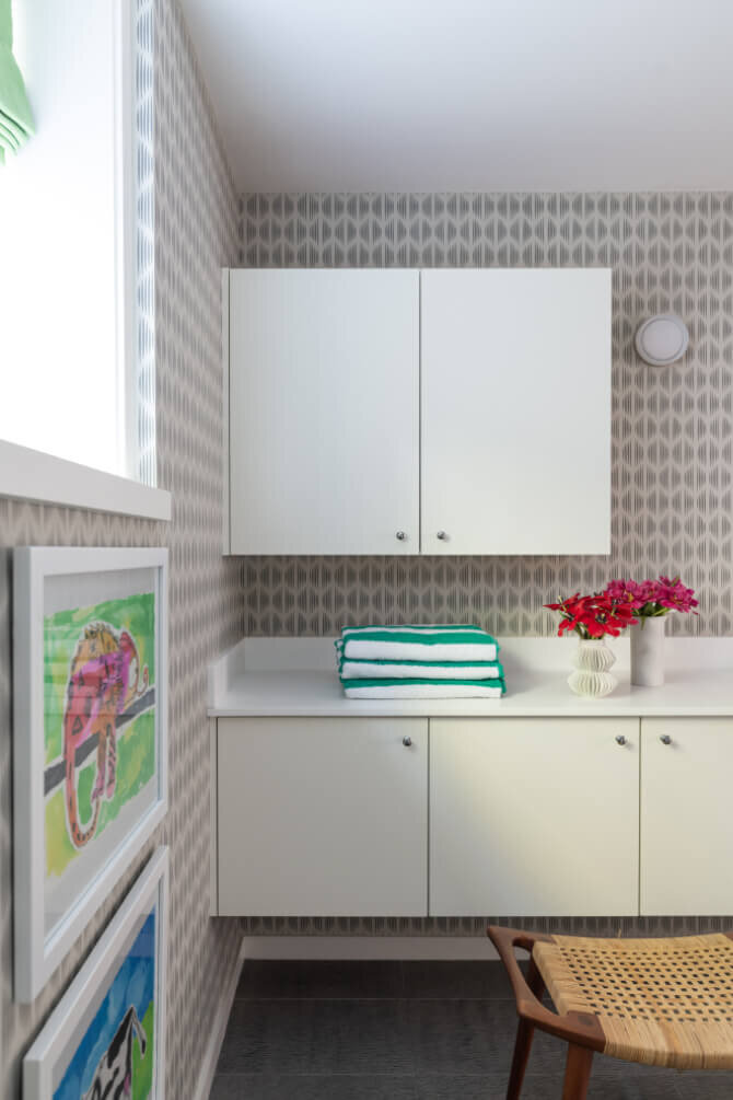Interior designers in Hingham, MA, create a kid-friendly basement with a white vanity, Schumacher wallpaper, and playful art, blending style and function.