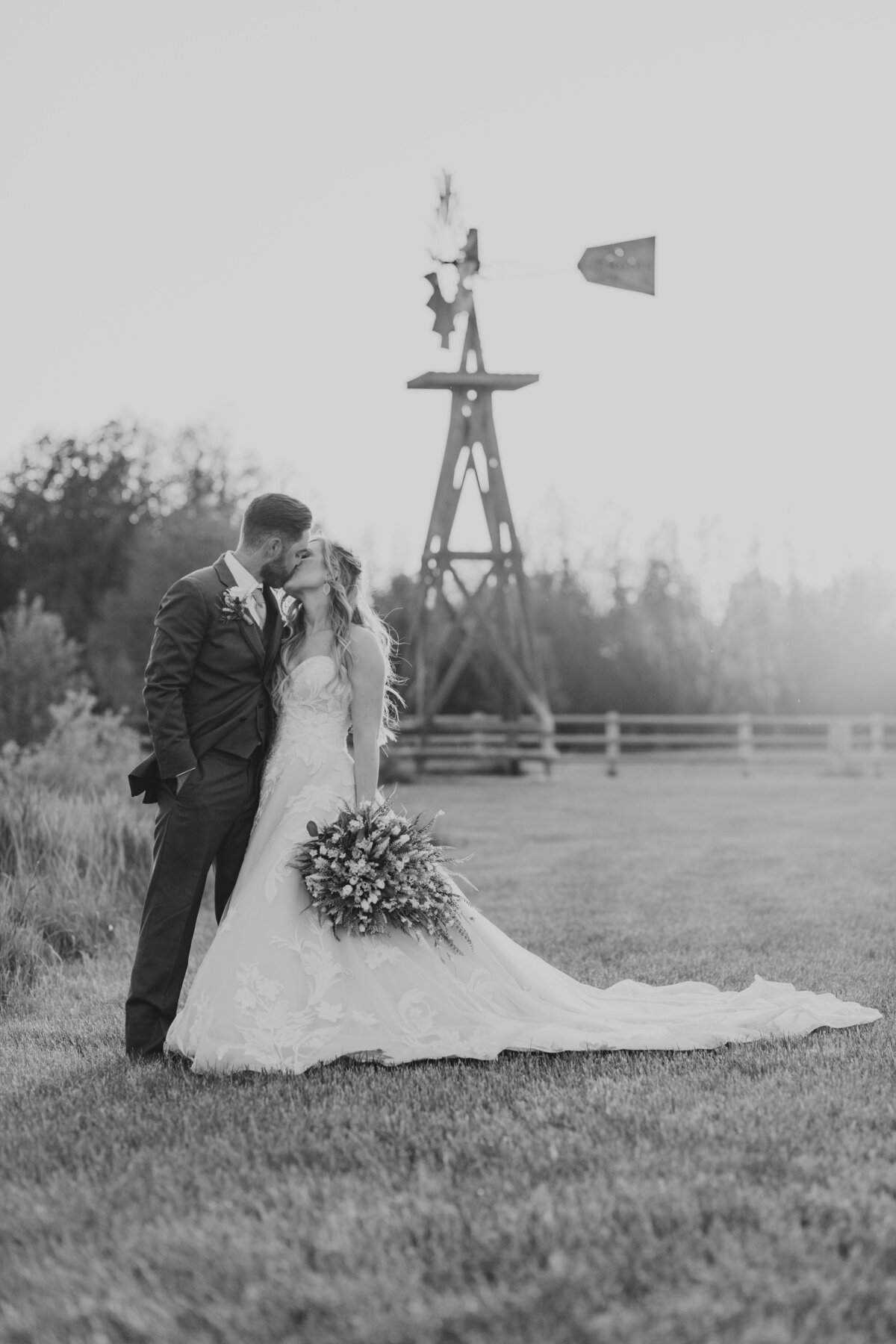black and white image bride and groom kissing by windmill