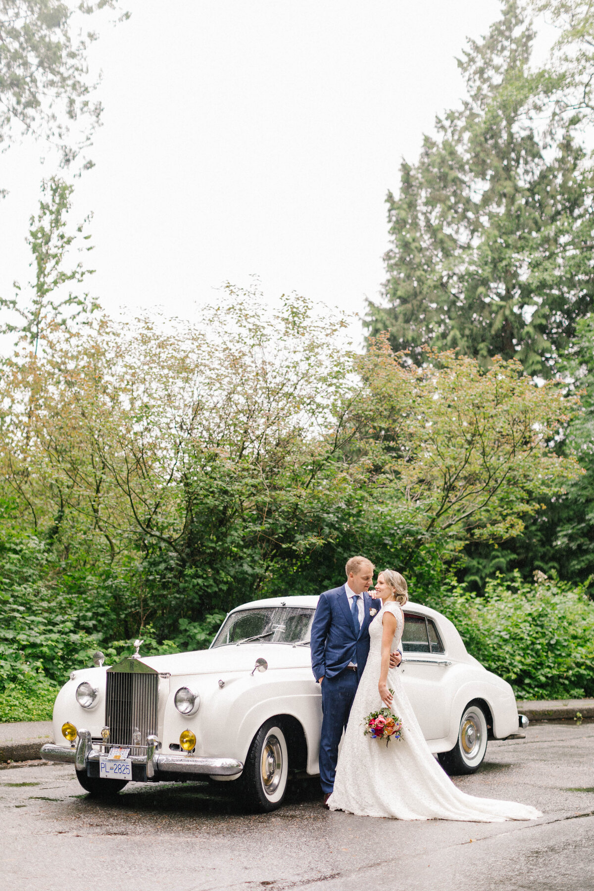 Bride and groom standing together in front of a vintage white car