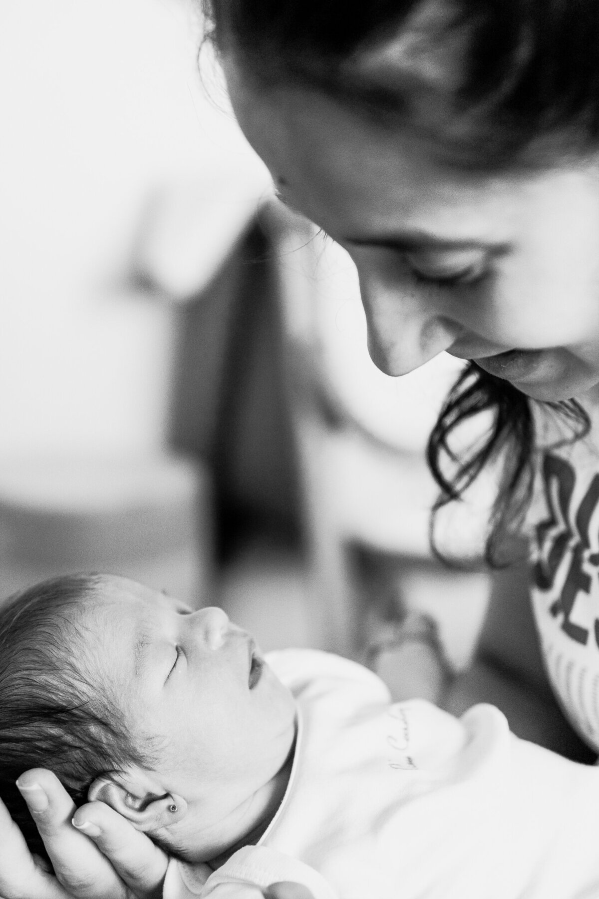 A black and white photo of a smiling woman gazing at a newborn baby she is cradling in her arms.