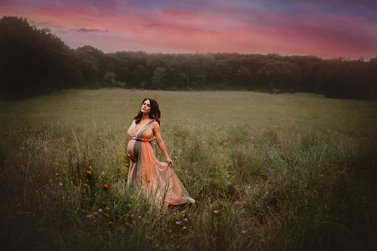 Mother in rainbow dress holding baby belly as sunset