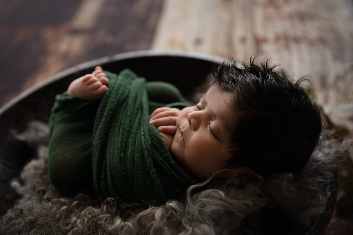 newborn boy in emerald green wrap asleep and has lots of hair