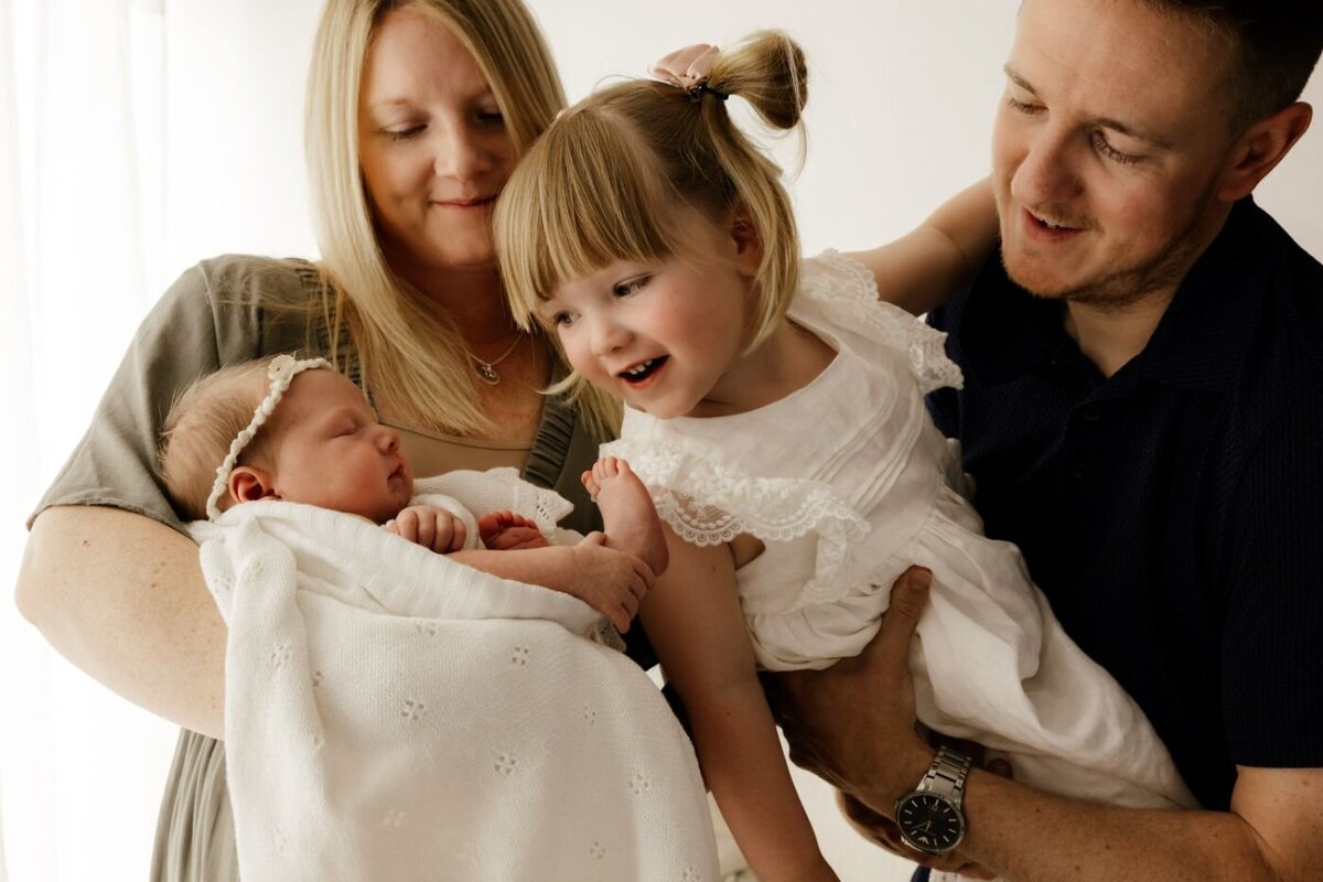 Parents adoringly hold their newborn baby and laughing older daughter. Lifestyle family photography