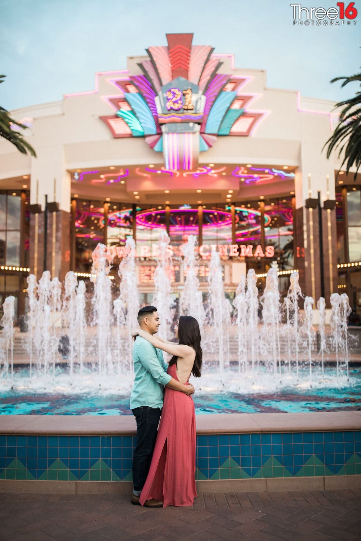 Engaged couple gaze at each other as they embrace in front of the dancing waters at Irvine Spectrum