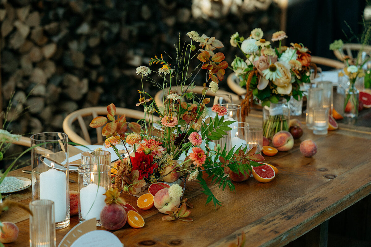 Bright, organic centrepieces of orange flowers decorate a wooden table at a Hoogan et Beaufort wedding reception. 
