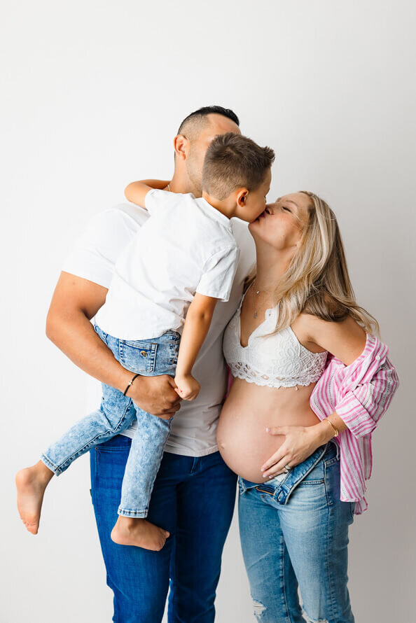 A little boy reaches over to kiss his mom who is touching her pregnant belly.