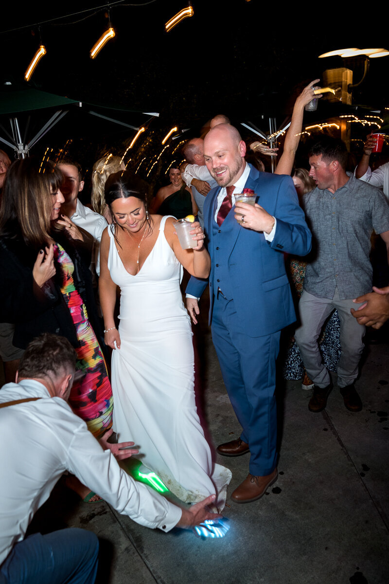A lively and fun moment as a groomsman proudly displays the bride’s light-up shoes while she enters the dance floor with the groom at Mitchell Grove, capturing the energy and excitement of the celebration.