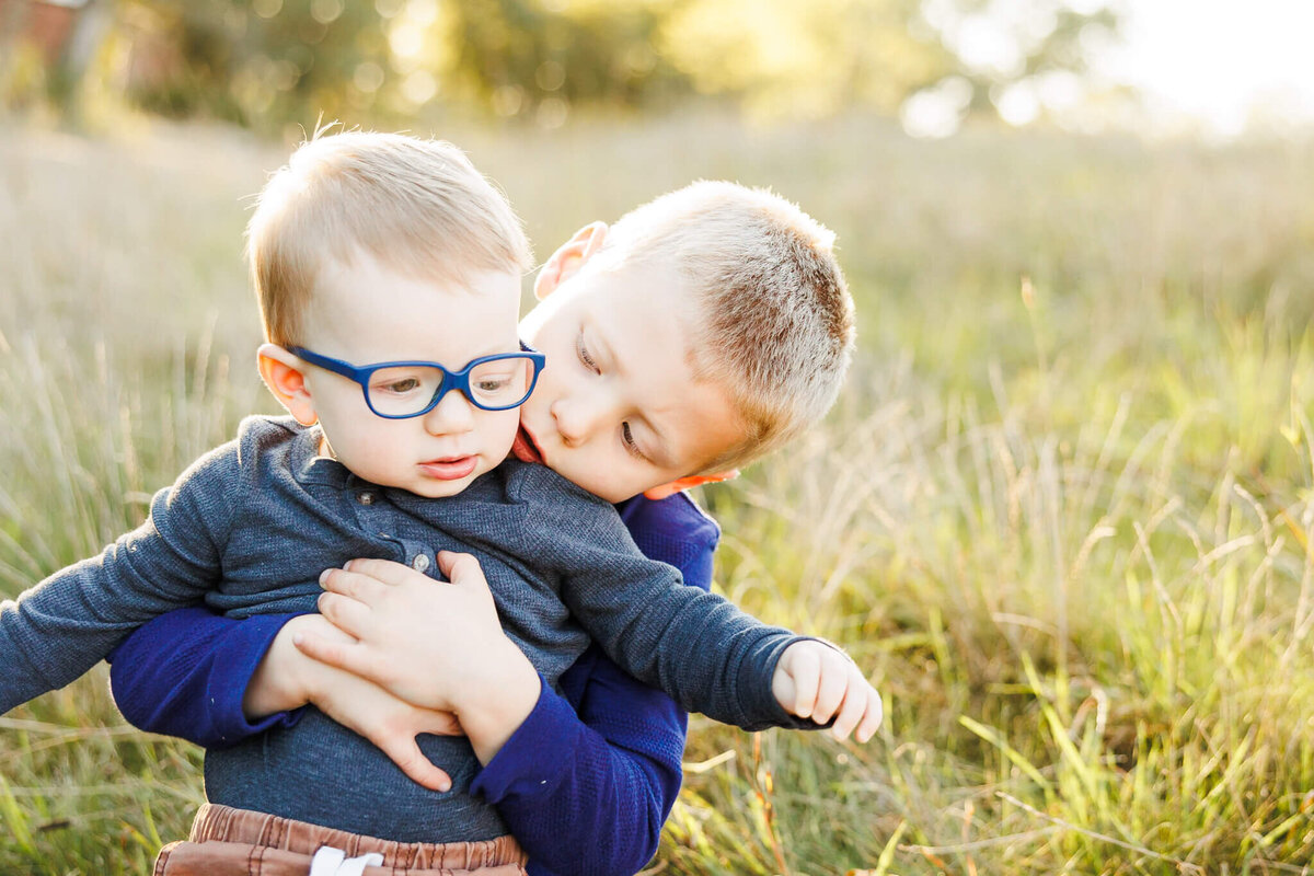 Older brother helping younger brother sit up in a field at Cantigny Park in Wheaton, IL.