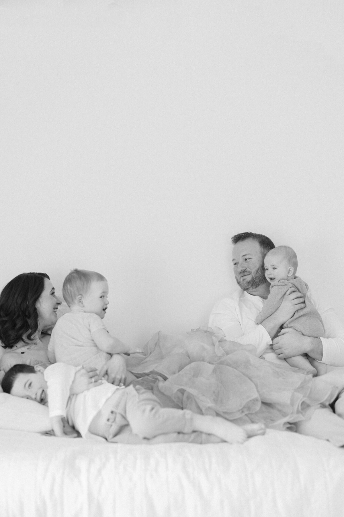Family snuggling on bed in all white studio laughing and playing by NJ Newborn Photographer