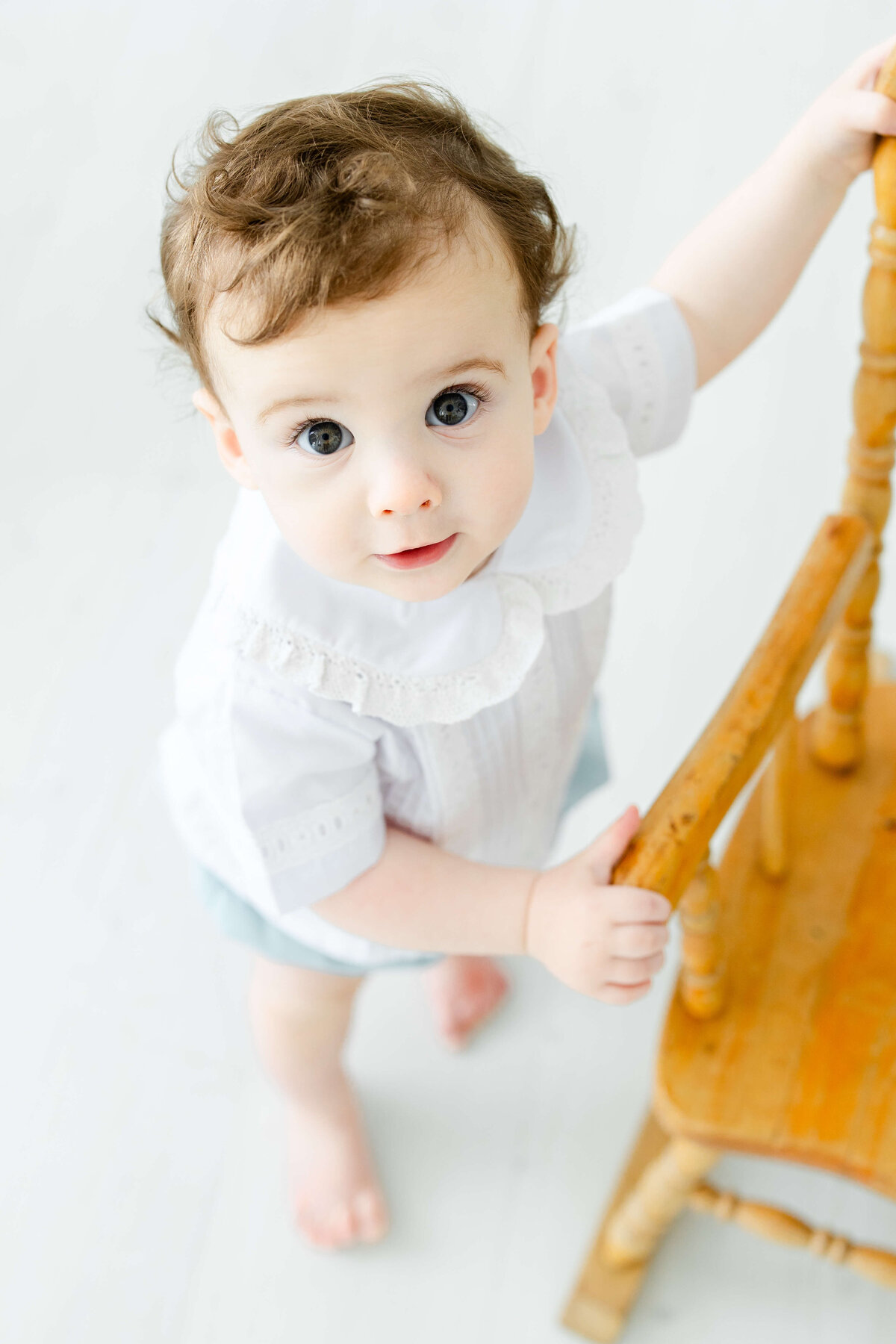 toddler standing up holding chair smiling at the camera for milestone photography