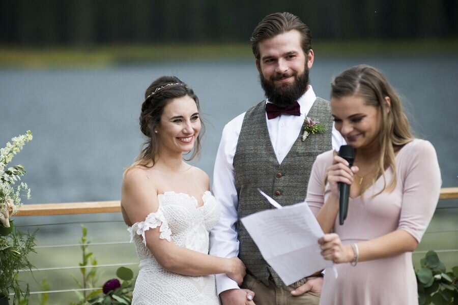 A bride and groom watch admiringly as a bridesmaid does a reading during their wedding ceremony.