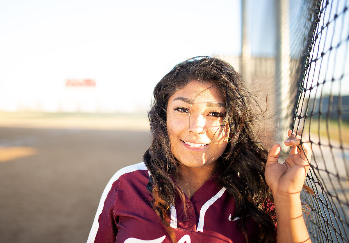senior softball girl smiling while holding field net