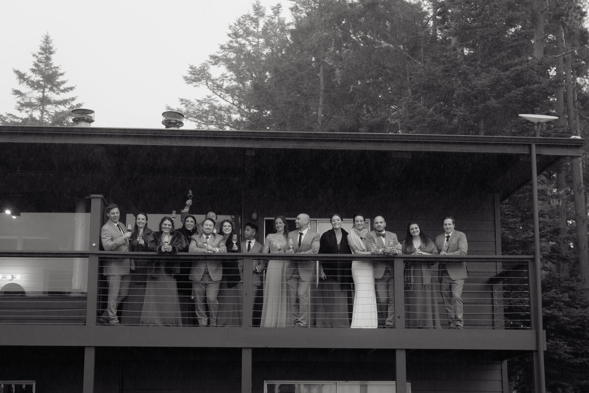 Black and white documentary wedding photography capturing a celebratory moment as guests toast on a balcony overlooking a serene forest, elegantly captured by a luxury documentary-style wedding photographer.