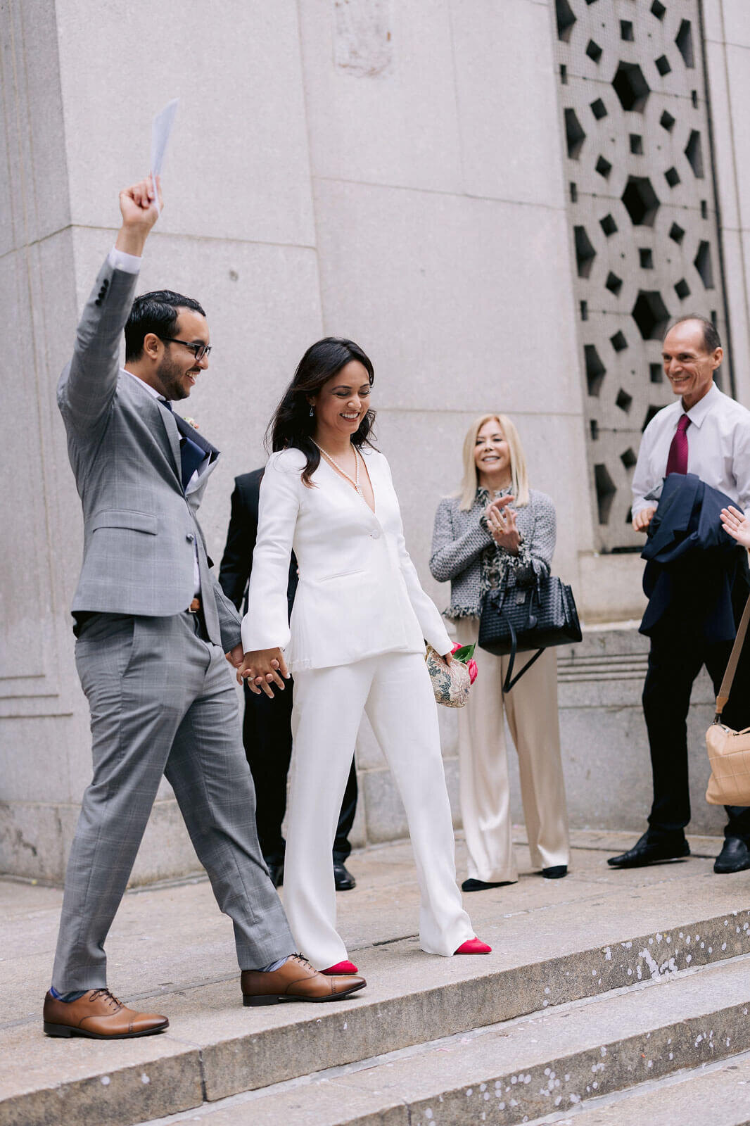 The bride and groom, walking hand in hand, happily exited NY City Hall, as their friends happily watch. Image by Jenny Fu Studio