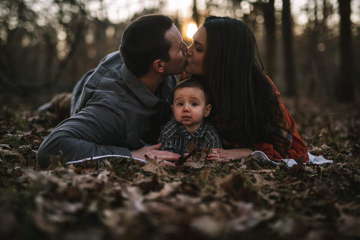 Couple kiss over baby as he stares at the camera.