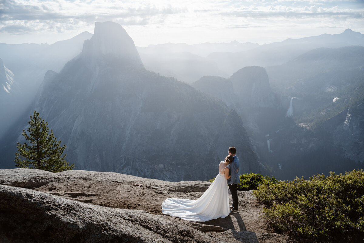 Newlywed couple standing close together and looking off toward the mountains