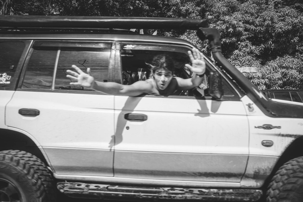 black and white image of man hanging out of car going by